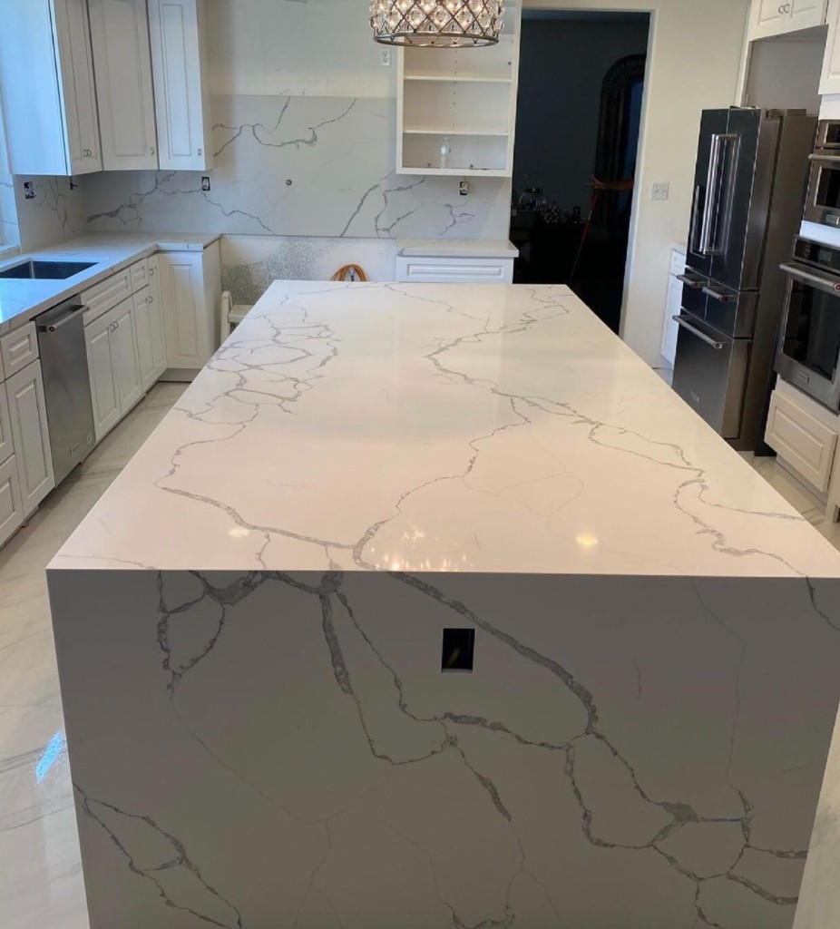 Waterfall kitchen island with full-height stone backsplash and wall ovens